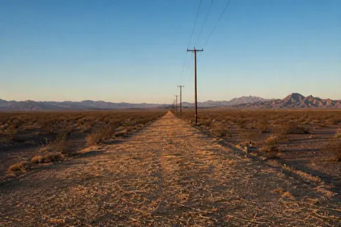 Long mulched utility corridor running straight across creosote flats near Yuma, power poles receding in one-point perspective